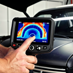 ** A mechanic using a thermal camera to inspect a car engine in a brightly lit garage. Focus on the thermal image on the camera's screen showing hotspots.

**